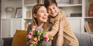 Hijo abrazando a madre después de regalar flores