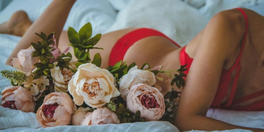 Donna in bikini rosso a due pezzi sdraiata sul letto accanto a rose bianche e rosa