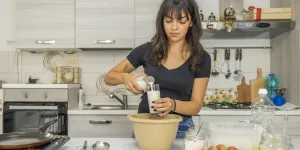 Femme versant du lait dans un verre pour préparer des crêpes