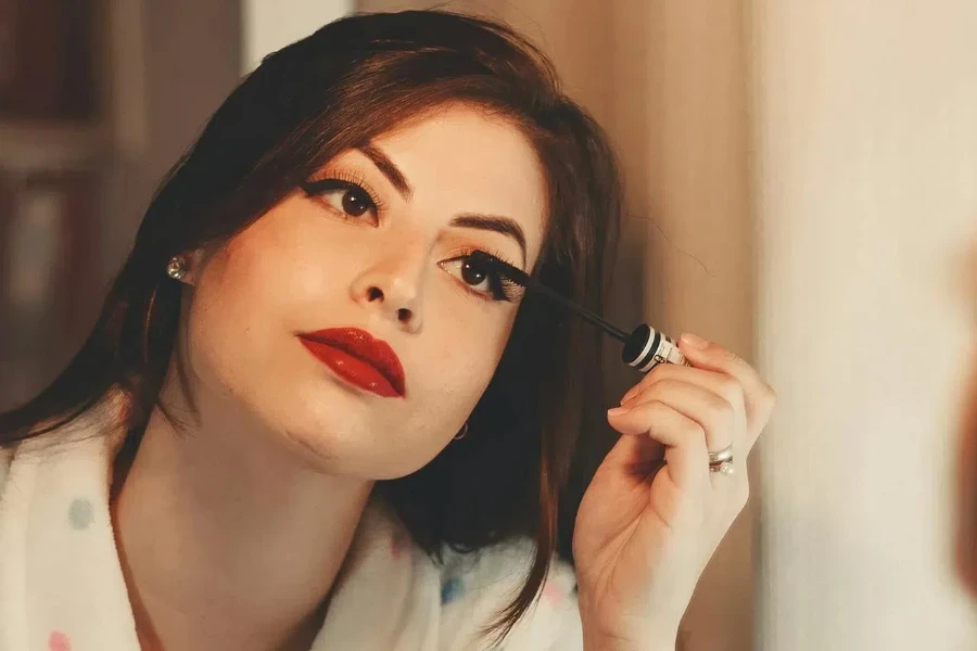 A beautiful woman applying mascara while wearing bold lipstick