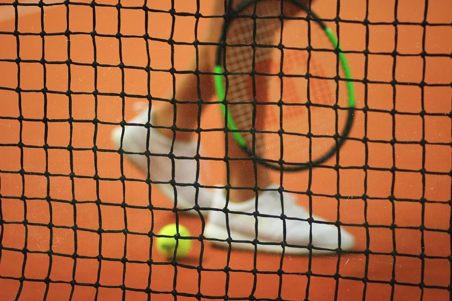 persona che indossa un paio di scarpe da ginnastica bianche basse mentre tiene in mano una racchetta da tennis Wilson