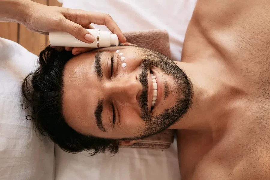 Terapeuta de spa aplicando crema humectante en el área debajo de los ojos de un hombre