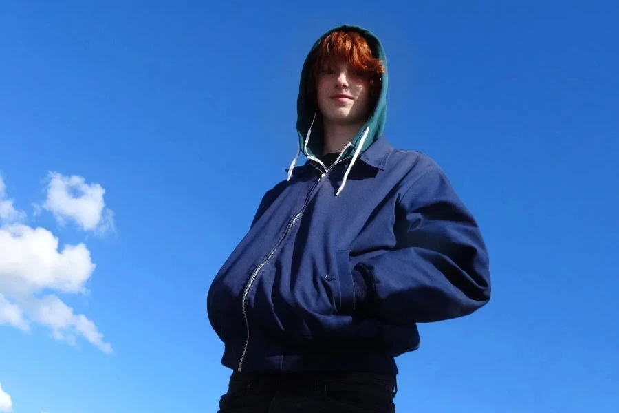 Un adolescent portant une veste Harrington bleue et un sweat à capuche vert