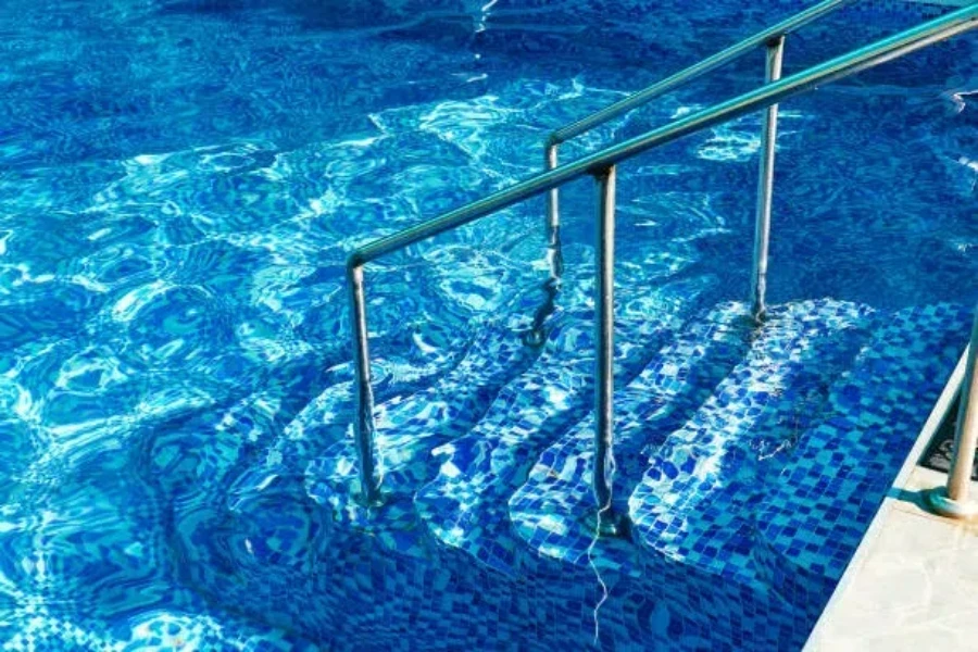 Degraus de piscina de azulejos com corrimão de metal indo para a piscina