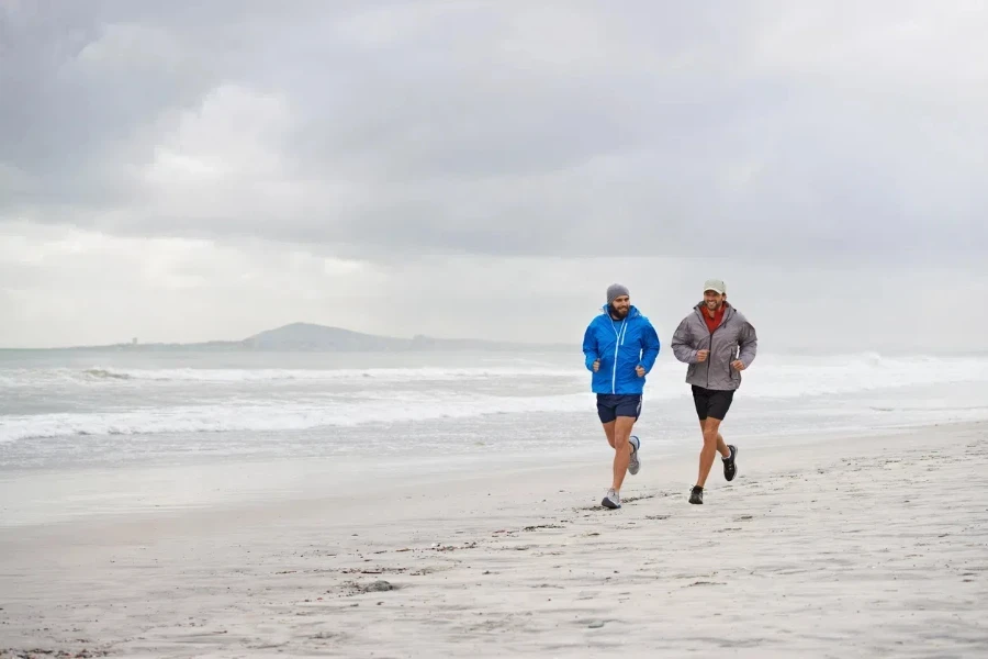 Dois homens com jaquetas Harrington correndo pela praia