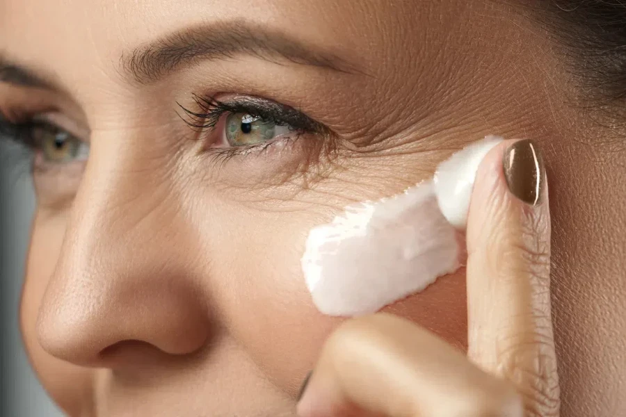 Mujer aplicando crema humectante en las líneas finas alrededor de los ojos.