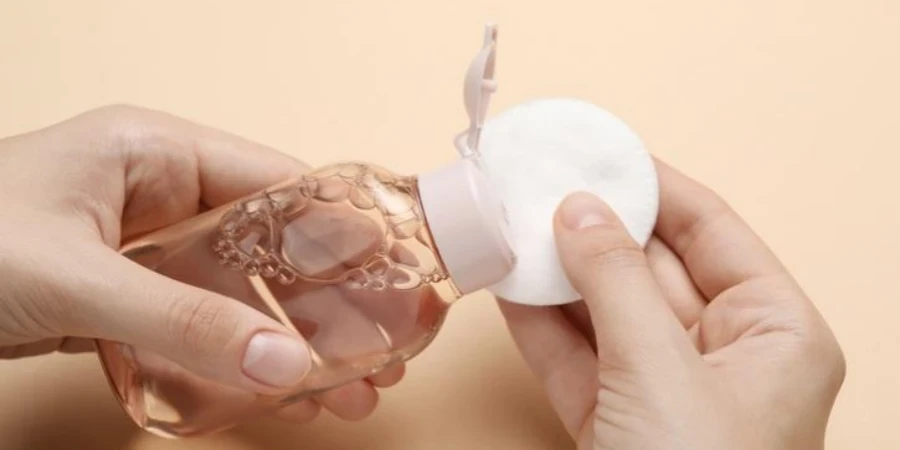 woman pouring micellar water from bottle onto cotton pad against beige background