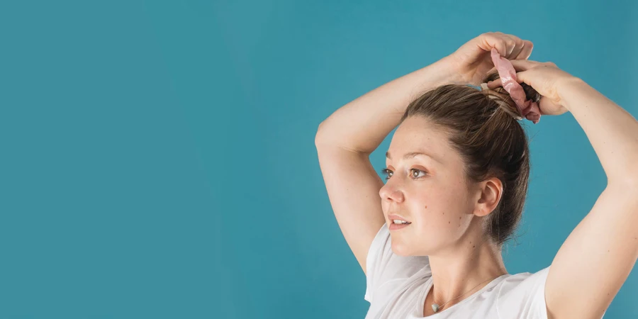 Una donna che si lega i capelli con uno scrunchie rosa