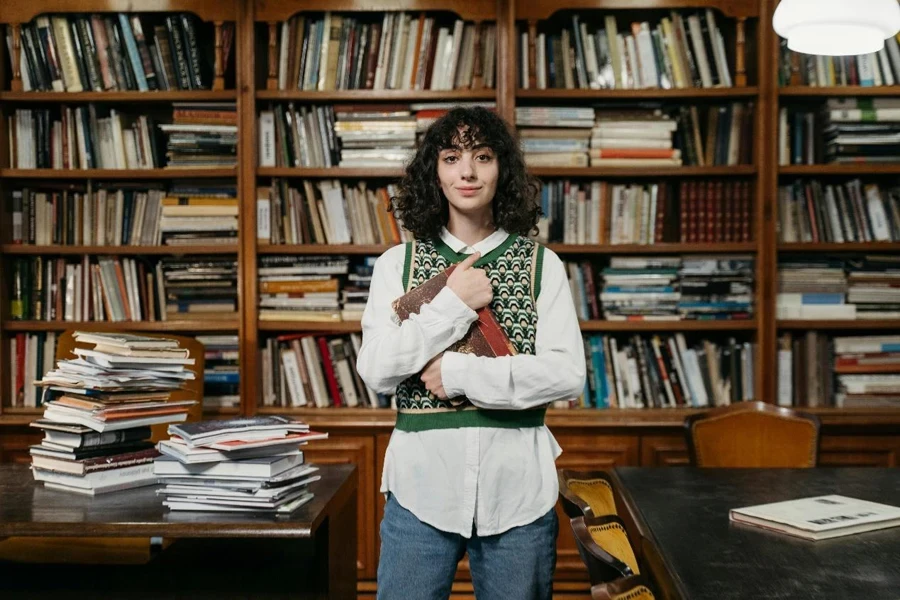 Una donna che indossa un gilet sopra una camicia elegante e tiene in mano un libro