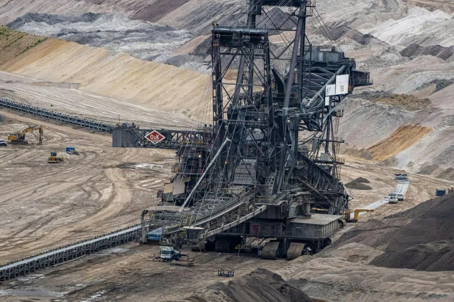 A bucket wheel excavator next to a road and cars shows the scale