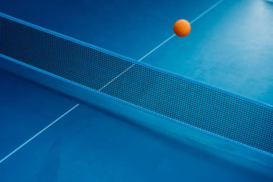 Pelota de tenis de mesa de color naranja que cruza la red sobre la mesa