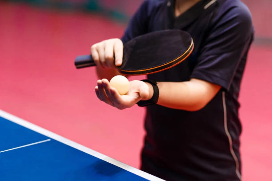 Persona sosteniendo una paleta y una pelota de tenis de mesa para servir