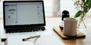 macbook na mesa com notebook e caneca de café