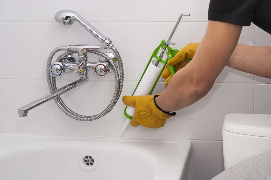 Un hombre aplicando sellador alrededor de una bañera.