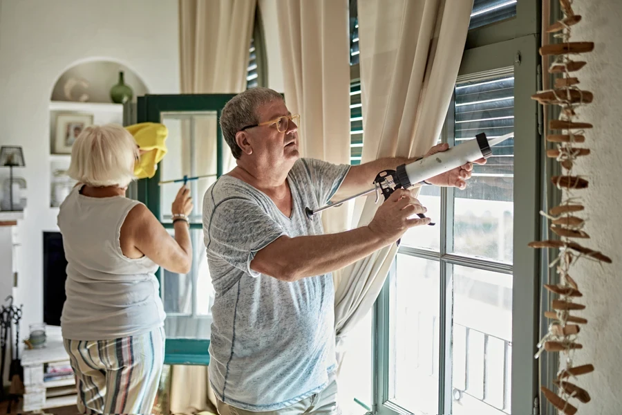 A man using a caulk gun to insulate windows