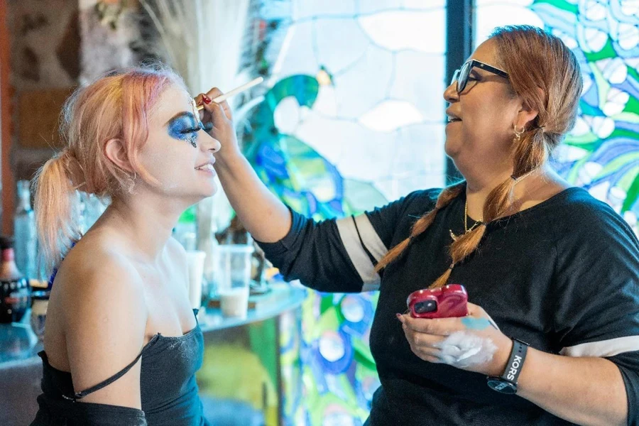 Eine Frau mit schwarzem Make-up und rosa Haaren lässt sich schminken