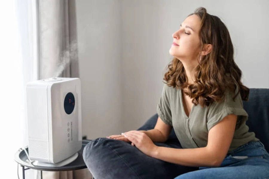 Atractiva mujer joven de cabello rizado que usa un humidificador de aire en casa