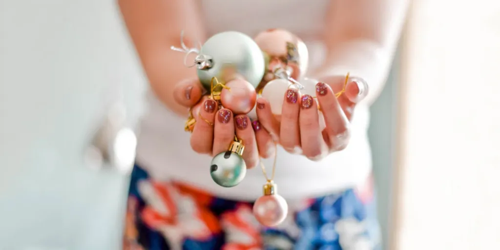 Mãos com unhas de Natal segurando vários enfeites de árvore