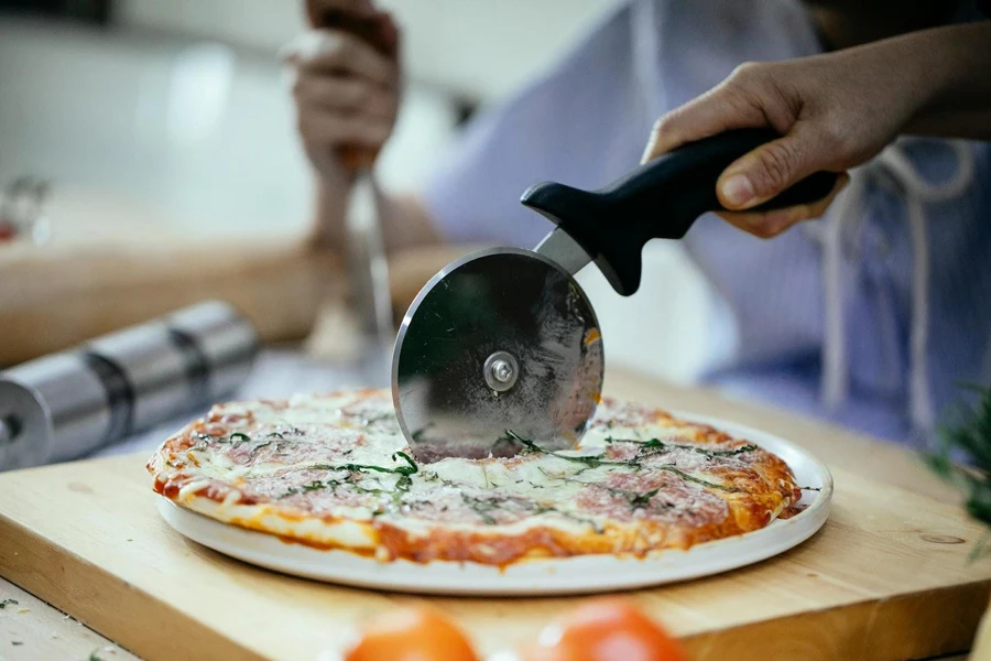 Pessoa usando um cortador de pizza em uma pizza caseira