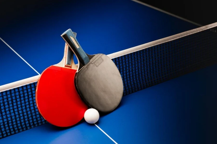 Mavi bir masanın üzerinde ağ bulunan ping pong raketleri ve topları