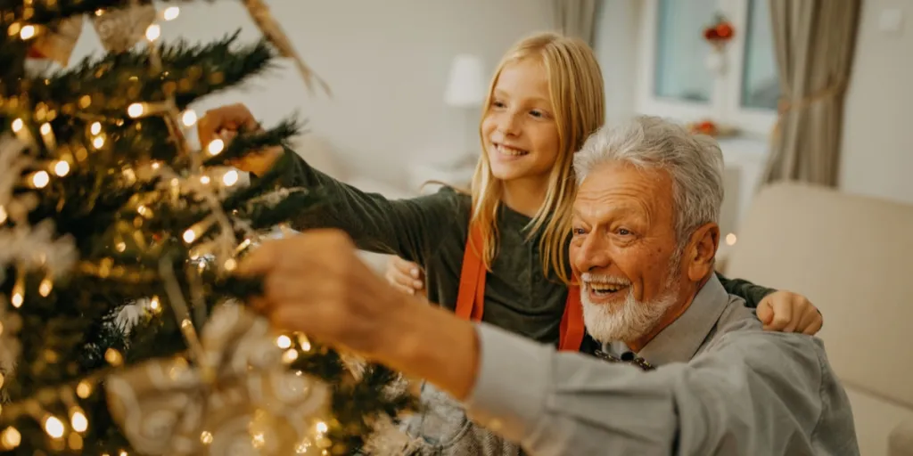 Homem idoso e neta decorando uma árvore de Natal