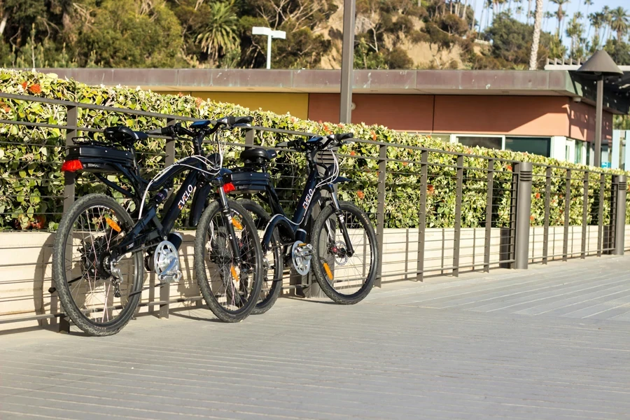 Duas bicicletas elétricas estacionadas em um corrimão ao lado de uma cerca