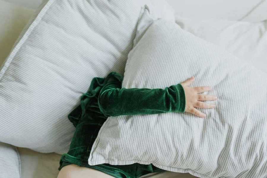 Unrecognizable child hiding face under pillow on bed