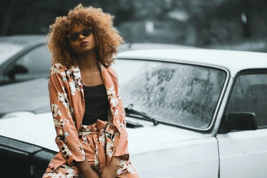 Femme portant un manteau et un pantalon à imprimé floral marron assise sur une voiture