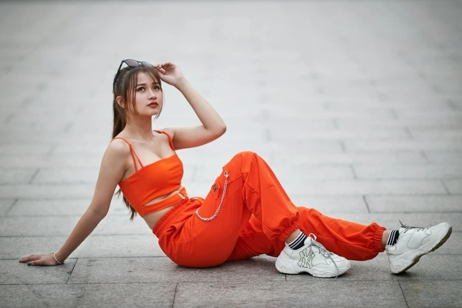 Woman in Sunglasses and an Orange Outfit Sitting on Pavement