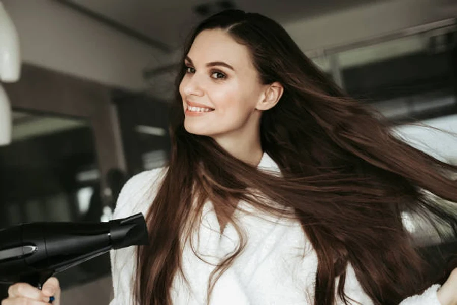 Mujer joven alegre secándose el cabello con secador