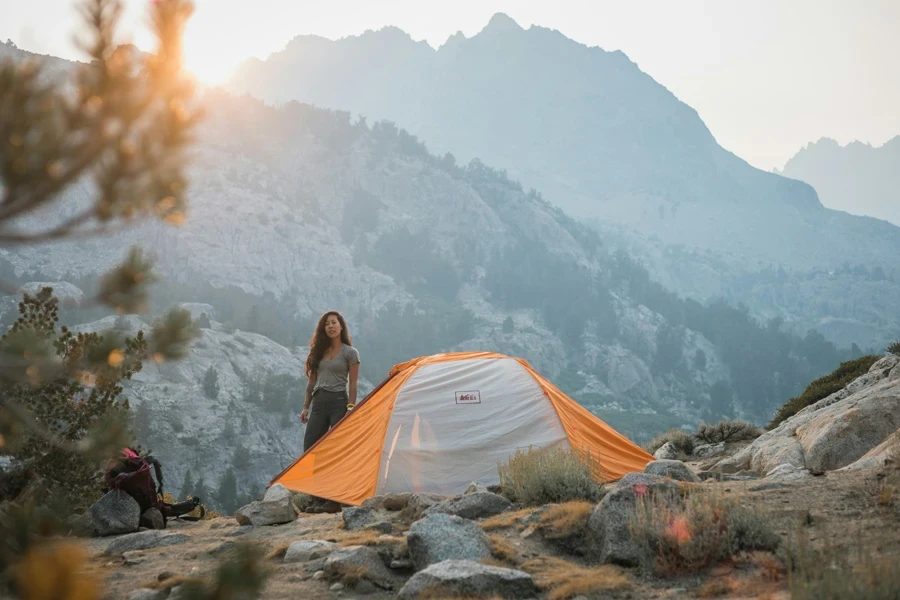 donna in giacca grigia seduta su una tenda grigia che guarda le montagne durante il giorno