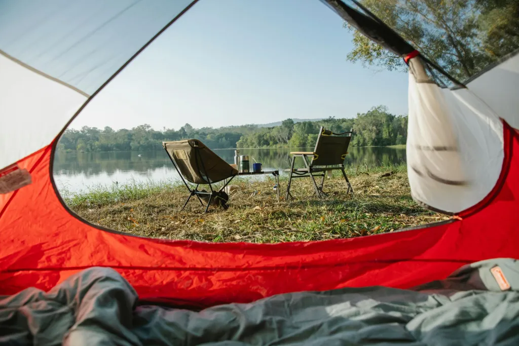 Vista rilassante del campeggio da una tenda vicino a un lago tranquillo con sedie sotto un cielo limpido