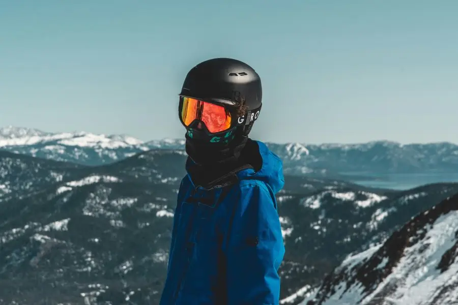 una persona che indossa un casco e degli occhiali protettivi in ​​piedi sulla cima di una montagna innevata