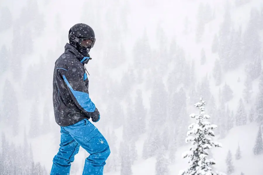 Snowboarder con equipaggiamento Spyder e casco K2 su una sporgenza innevata