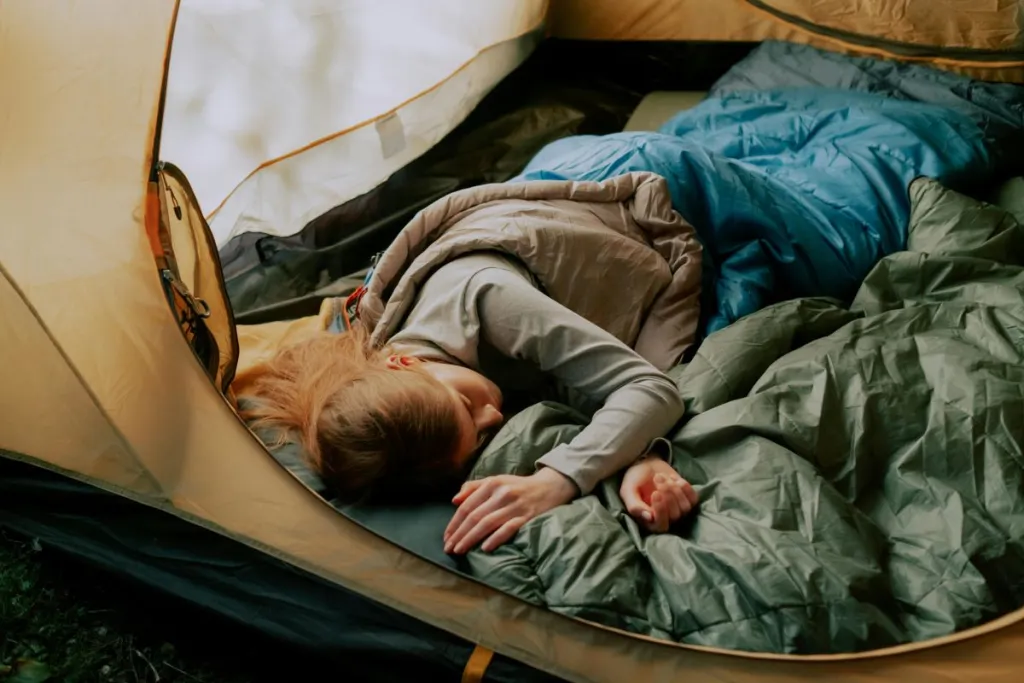 una donna che dorme comodamente in una tenda durante un campeggio, circondata dalla natura