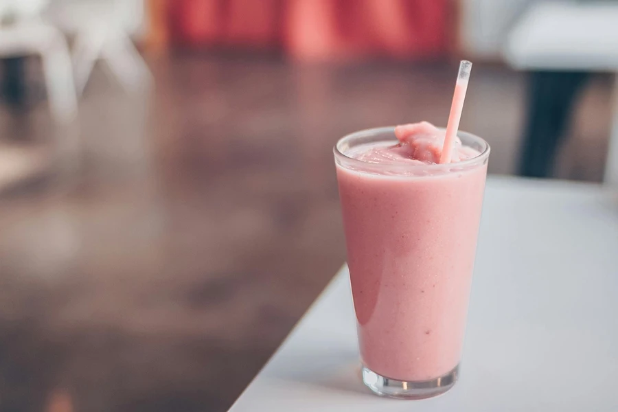 A glass of pink milkshake with a straw