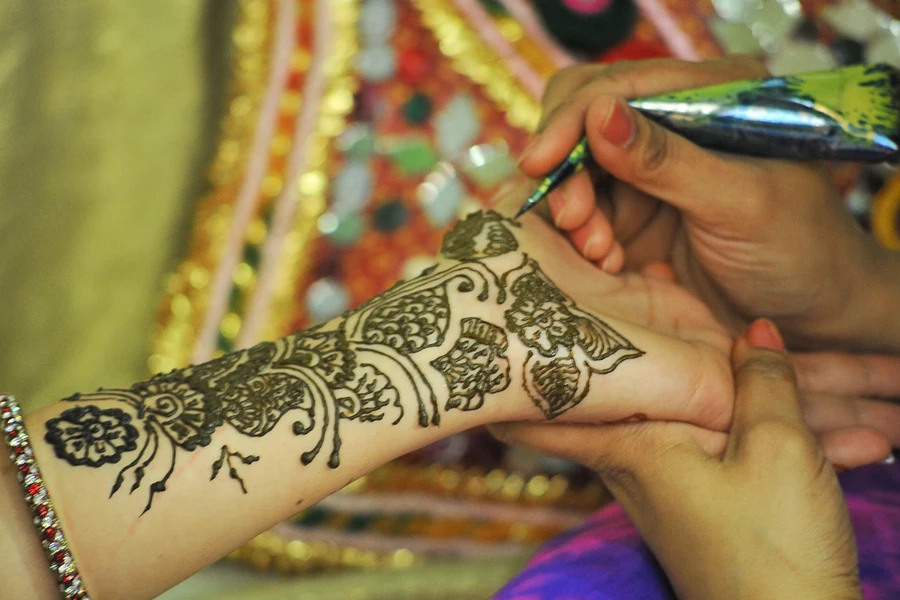 An artist drawing henna on a woman’s hand