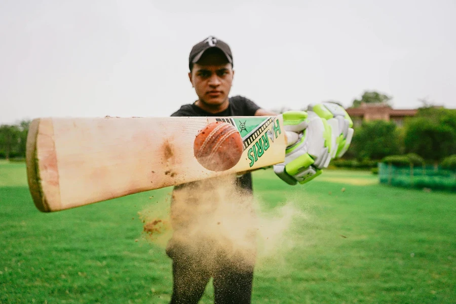 Primo piano della mazza da cricket e della palla colpita da uno sportivo che indossa abbigliamento sportivo e guanti