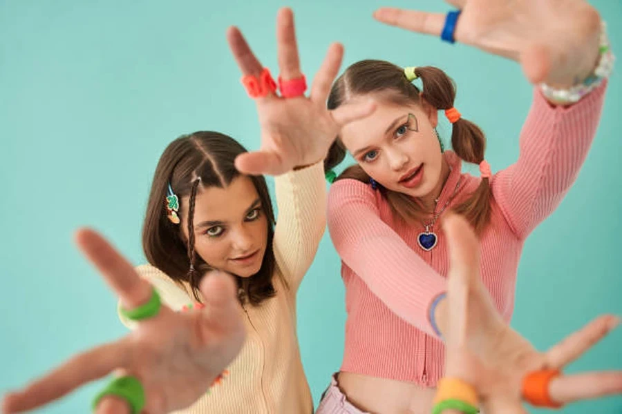 Girls Stretching Hands to the Camera While Posing at Bright and Creative Clothes