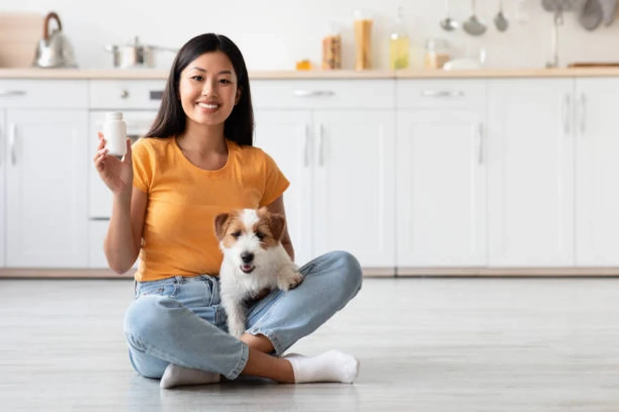 Senhora feliz com cachorrinho fofo mostrando pote de suplemento para animais de estimação