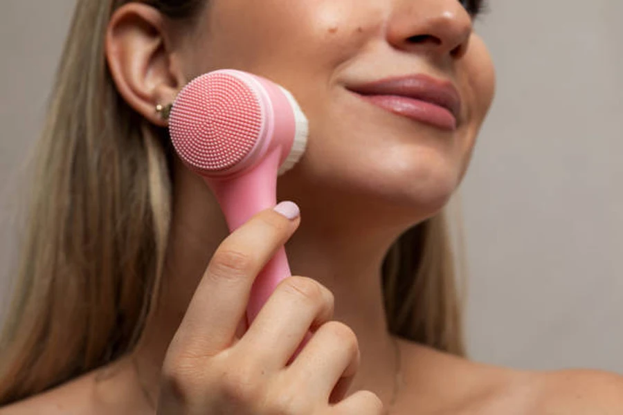 Pink and white makeup cleansing brush used on cheek