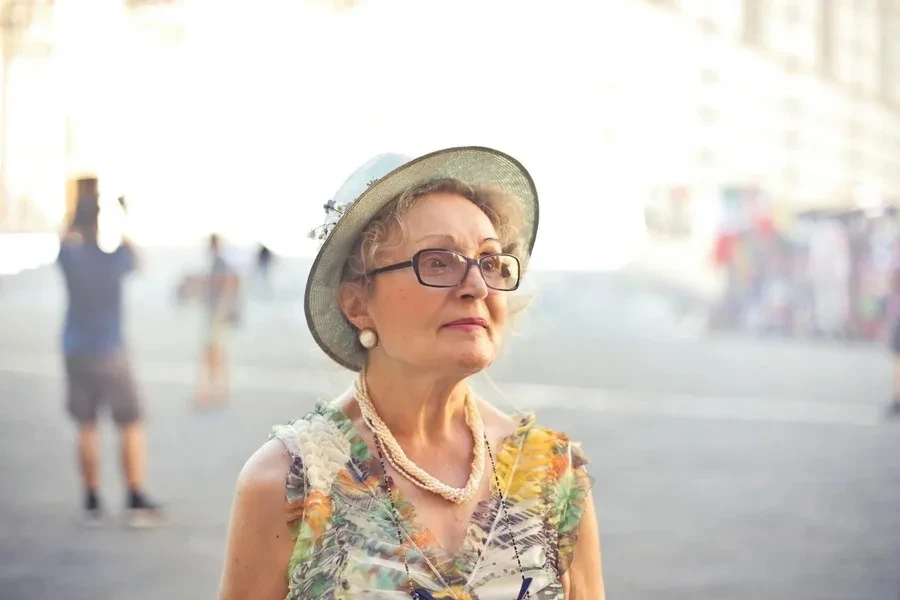 Una anciana con cabello corto parada en un campo con un vestido pastel.