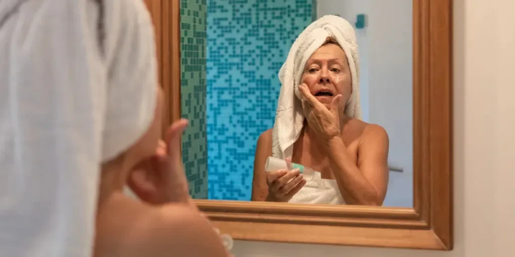 74 years-old argentinean senior lady doing her facial beauty routine in front of the mirror at bathroom