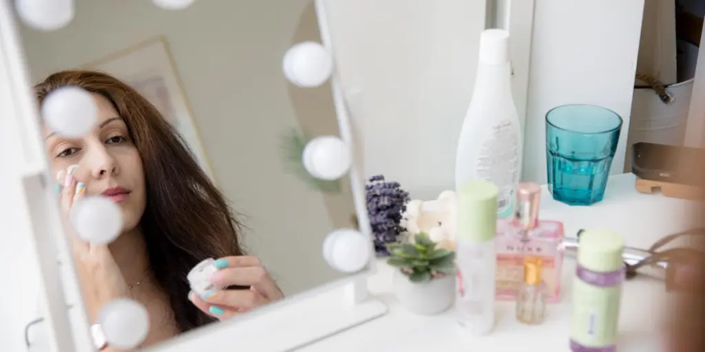 A Person Looks Into A Mirror Rubbing In Face Cream