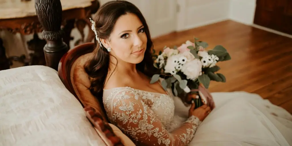 A beautiful bride in a lace gown holding a bouquet at an indoor wedding setting