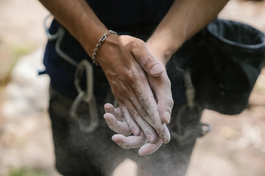 Un primo piano delle mani di un adulto ricoperte di polvere di gesso, pronte per l'arrampicata su roccia