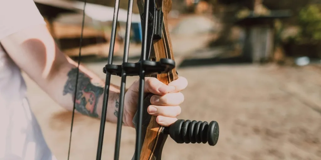 Una toma de primer plano de una mano tatuada agarrando un arco compuesto al aire libre en un día soleado.