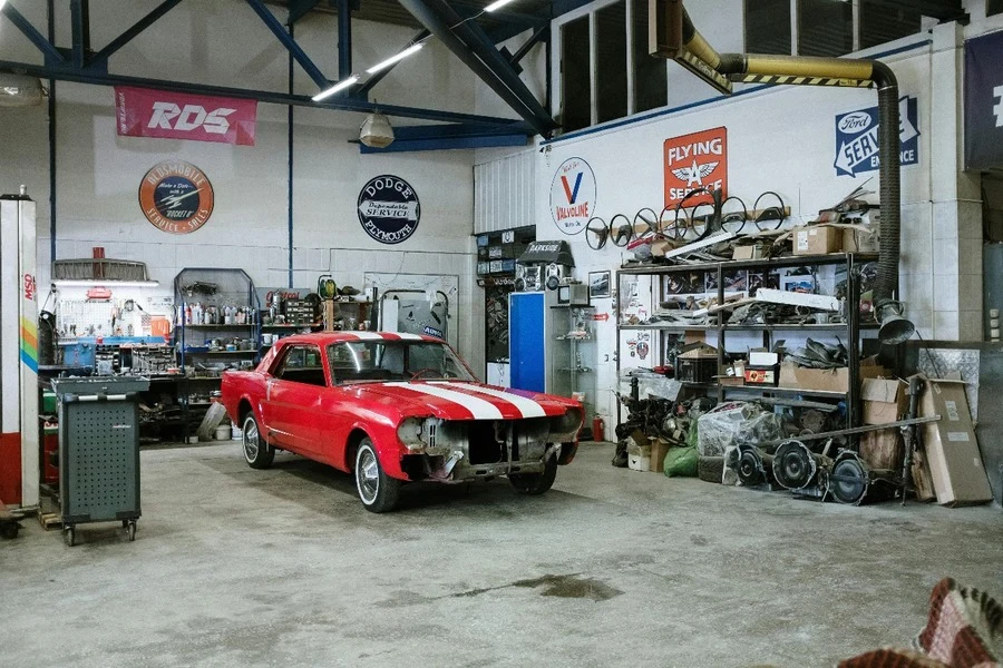 A cluttered garage with a vintage red car parked inside