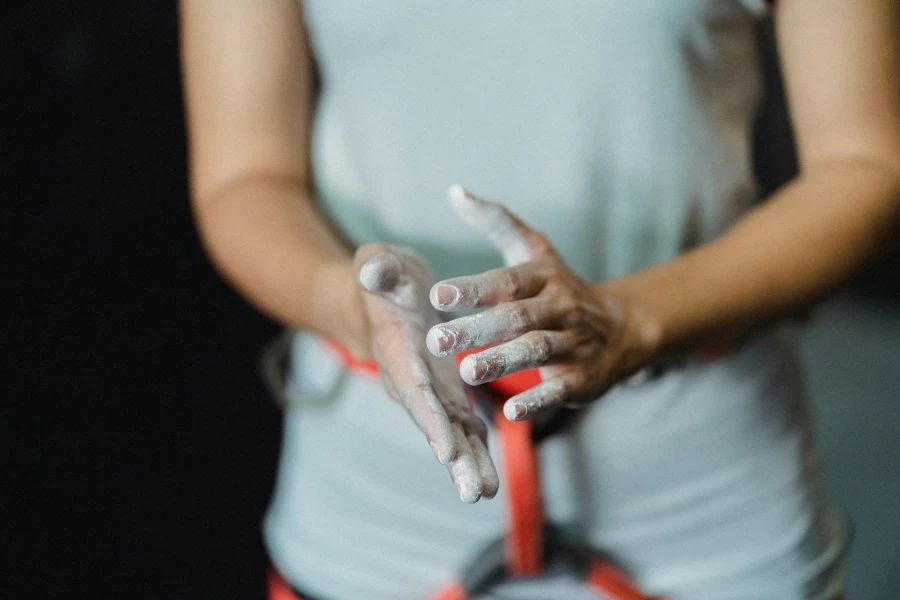 A female climber prepares by applying chalk to her hands before a climb indoors