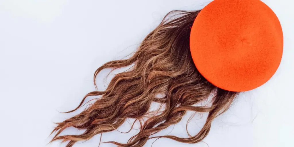 A flat lay image showcasing an orange hat with flowing brown hair against a white background